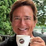 Person smiling, holding a coffee cup outdoors.